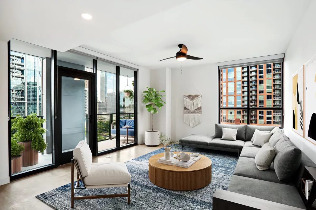 Living room with large windows, a grey sectional sofa, wooden coffee table, and outdoor access to a balcony.