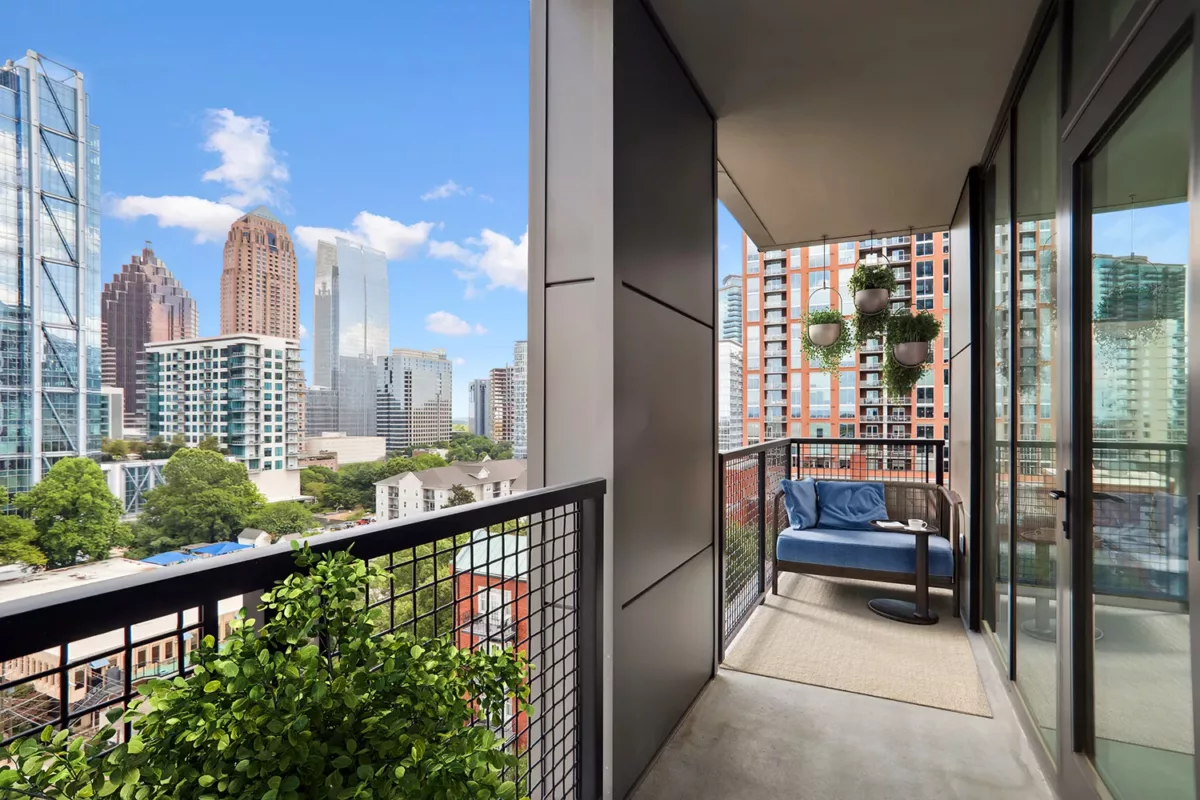 Balcony with a blue cushioned chair, potted plants, and a view of skyscrapers.