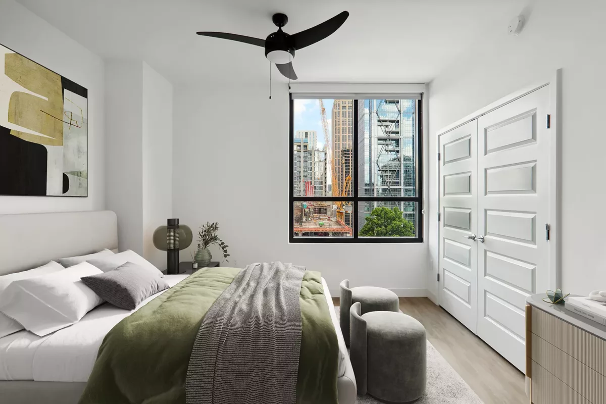 Cozy bedroom with a green throw blanket on the bed, abstract artwork, and city view through a large window.