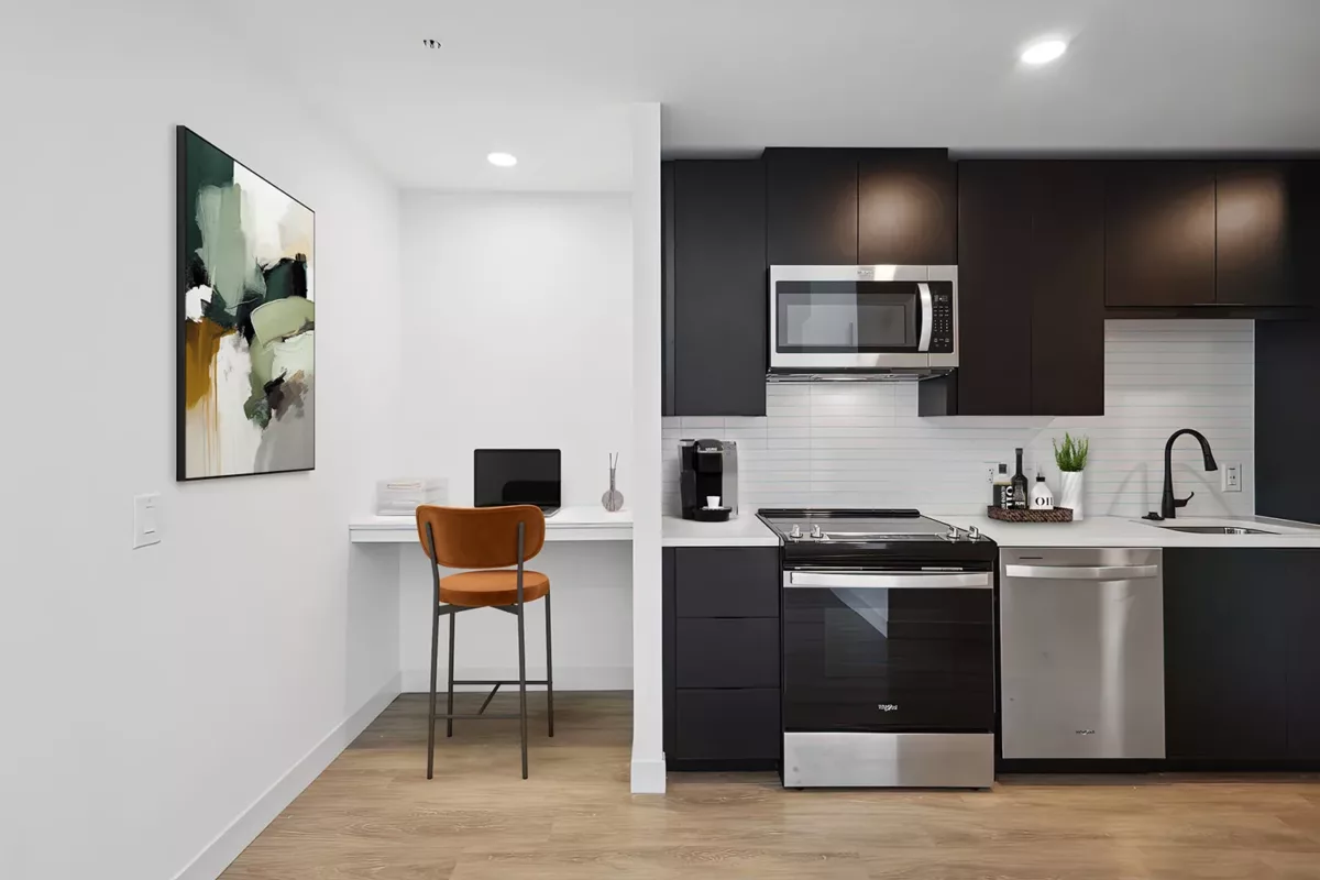 Kitchen with black cabinetry, stainless steel appliances, and a small adjacent desk with a chair.
