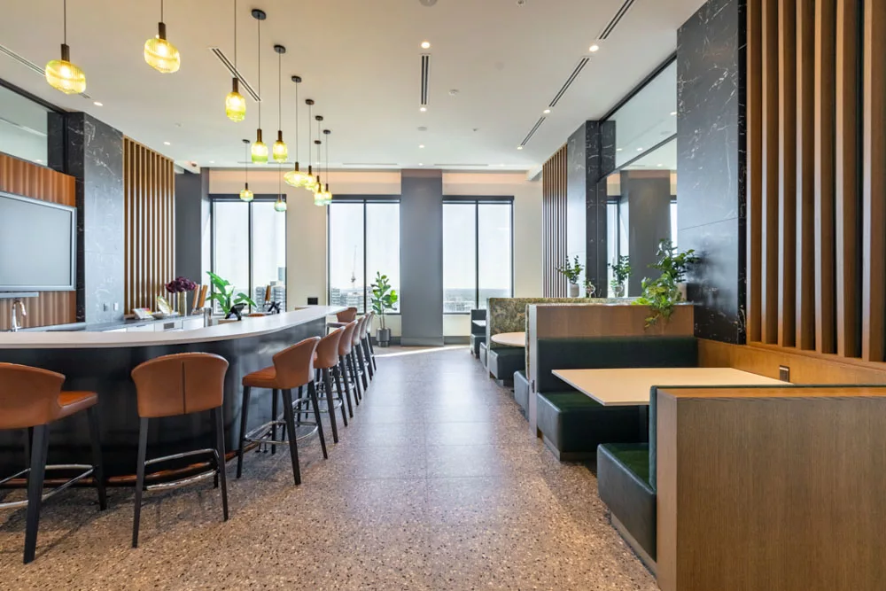 Contemporary bar area with a curved counter, leather barstools, booth seating, and pendant lighting.