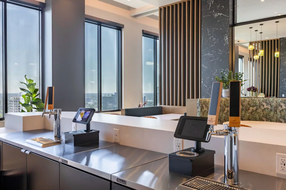 Close-up of self-serve taps with stainless steel counters in a bright lounge with large windows.