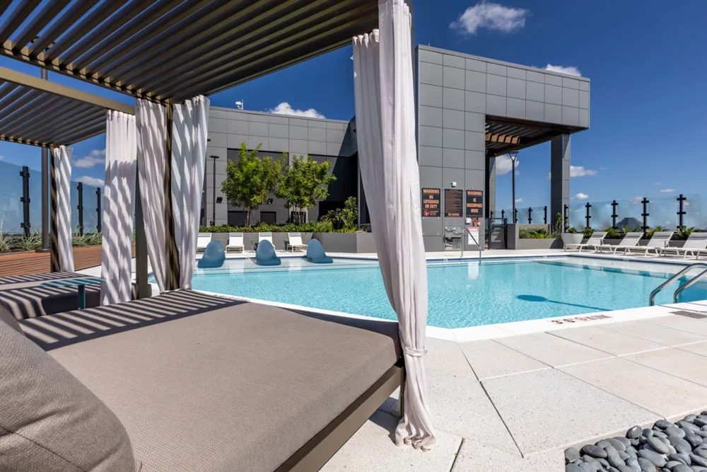 Rooftop pool with cabanas, lounge chairs, and a panoramic city view under a clear blue sky.