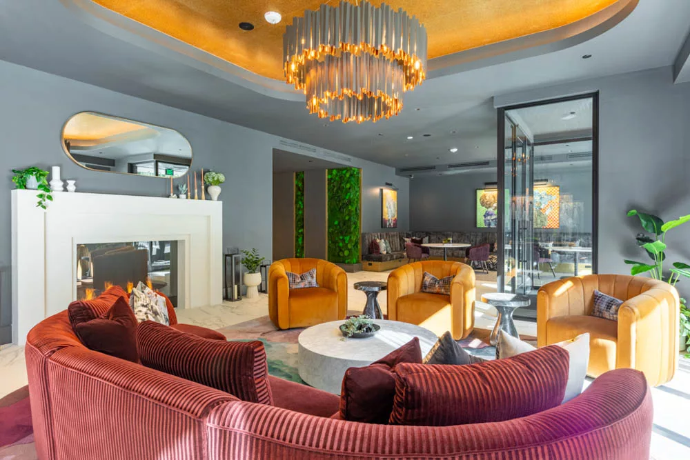 Cozy seating area with a burgundy sectional, mustard chairs, and a fireplace, featuring vibrant greenery and modern décor.